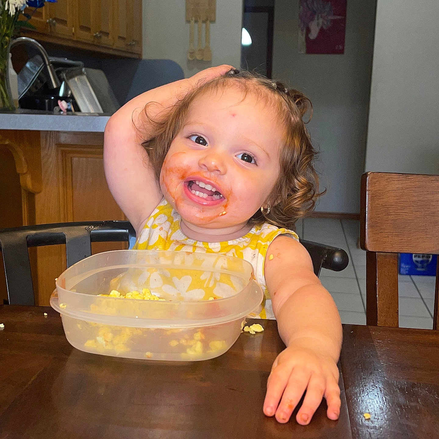 Meleah joined the competition — help win amazing prizes! cabinet, chair, child, curly_hair, cute, eating, food, happy, indoor, kitchen, messy_face, person, plastic_container, playful, popcorn, portrait, smiling, toddler, wooden_table, yellow_dress