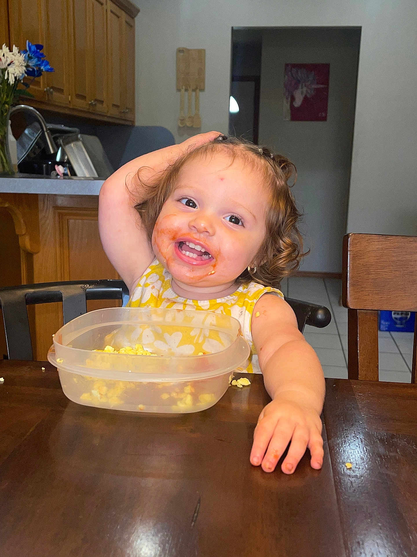 Meleah joined the competition — help win amazing prizes! cabinet, chair, child, curly_hair, cute, eating, food, happy, indoor, kitchen, messy_face, person, plastic_container, playful, popcorn, portrait, smiling, toddler, wooden_table, yellow_dress