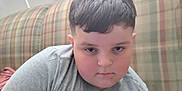 Malachi joined the competition — help win amazing prizes! blinds, boy, casual, child, couch, dinosaur_graphic, expression, face, furniture, grey_shirt, hair, home, indoor, person, plaid, portrait, relaxed, seated, window, young