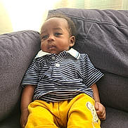 Kenny a rejoint le concours — aidez-le/la à gagner de superbes lots ! child, toddler, striped_shirt, yellow_shorts, couch, indoors, portrait, relaxed, casual_clothing, cartoon_print, natural_light, window_light, curtains, comfortable, young_child, seated, expression, home, soft_light, calm