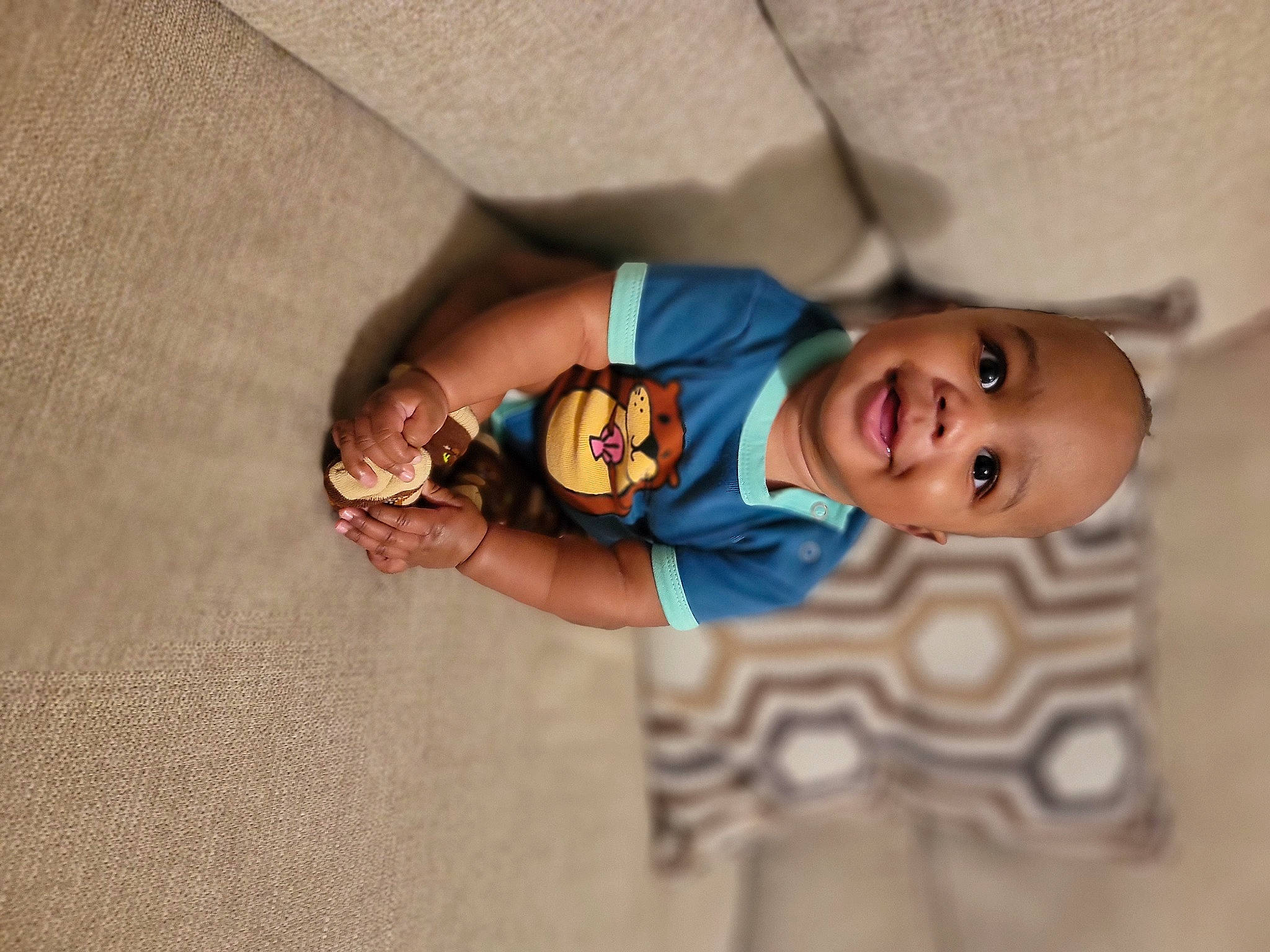 Kendrick is registered to the contest to win money with this photo: baby, baby_toddler_clothing, child, comfort, finger, floor, flooring, fun, happy, hardwood, joy, mammal, mouth, nose, person, room, skin, sleeve, smile, t_shirt