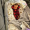 baby, newborn, sleeping, onesie, red_and_black_checkered, baby_nest, blanket, bassinet, floral_pattern, cozy, infant, soft_toys, sleep, rest, indoors, child, peaceful, cute, warm, comfortable