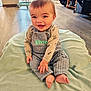 baby, child, smiling, sitting, blanket, overalls, long_sleeve, floor, wooden_floor, indoor, happy, person, face, feet, furniture, high_chair, home, cozy, cute, playful