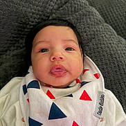 Naomi is registered to the contest to win money with this photo: baby, bib, black_hair, blanket, blue, child, clothing, cute, drool, eyes, face, indoors, infant, lying_down, mouth, pattern, portrait, red, texture, white