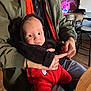 baby, child, person, holding, jacket, red_clothing, black_clothing, indoor, cafe, table, chair, neon_sign, neon_light, face, hands, seated, cute, fuzzy_outfit, drool, curious