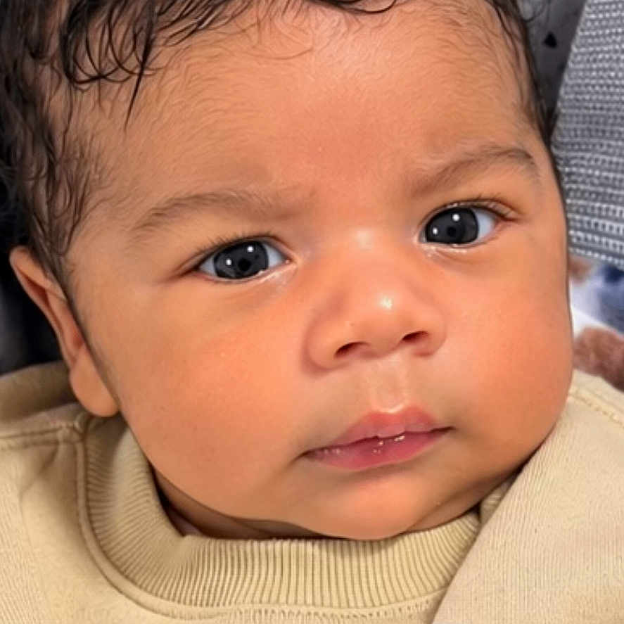 Jean Lucas joined the competition — help win amazing prizes! baby, infant, child, portrait, close_up, face, eyes, looking_at_camera, neutral_expression, curly_hair, brown_hair, sweatshirt, clothing, indoor, blanket, seated, phone_screenshot, lock_screen, clock, patterned_background