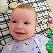 Shelby is registered to the contest to win money with this photo: baby, smiling, face, infant, blanket, toy, clothing, onesie, cute, happy, child, lying_down, indoor, closeup, head, expression, pattern, soft, playful, comfort