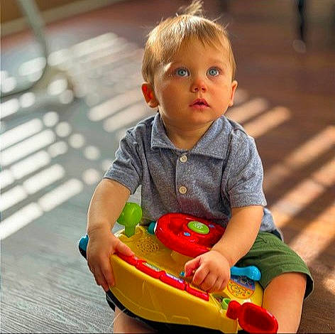 Logan is registered to the contest to win money with this photo: baby, baby_playing_with_toys, baby_toddler_clothing, cheek, child, flooring, fun, grass, happy, leisure, musical_instrument, person, photograph, recreation, riding_toy, sitting, skin, toddler, toy, toy_vehicle
