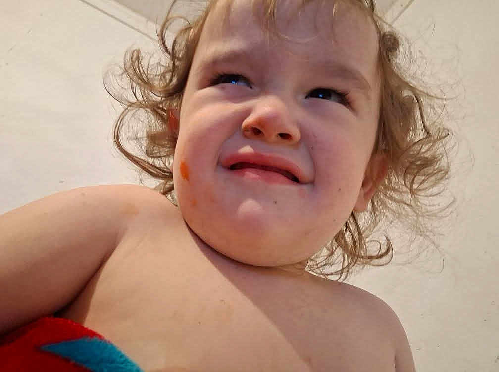 Oaklan is registered to the contest to win money with this photo: toddler, child, curly_hair, face, expression, food_stain, skin, bare_chest, person, portrait, closeup, messy_hair, confused, indoor, light_background, young_child, head, cheek, emotion, skin_tone