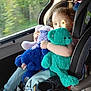 child, toddler, car_seat, stuffed_toy, blue_bear, green_bear, window, car_interior, sunlight, plush_toy, childrens_clothing, pants, seatbelt, travel, road_trip, nature, trees, daylight, cute, happy
