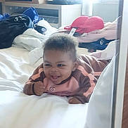 Jaylani is registered to the contest to win money with this photo: baby, infant, child, smiling, bed, blanket, pajamas, hotel_room, luggage, bra, window, mirror_reflection, pillow, furniture, happy, portrait, hair, face, cozy, tummy_time