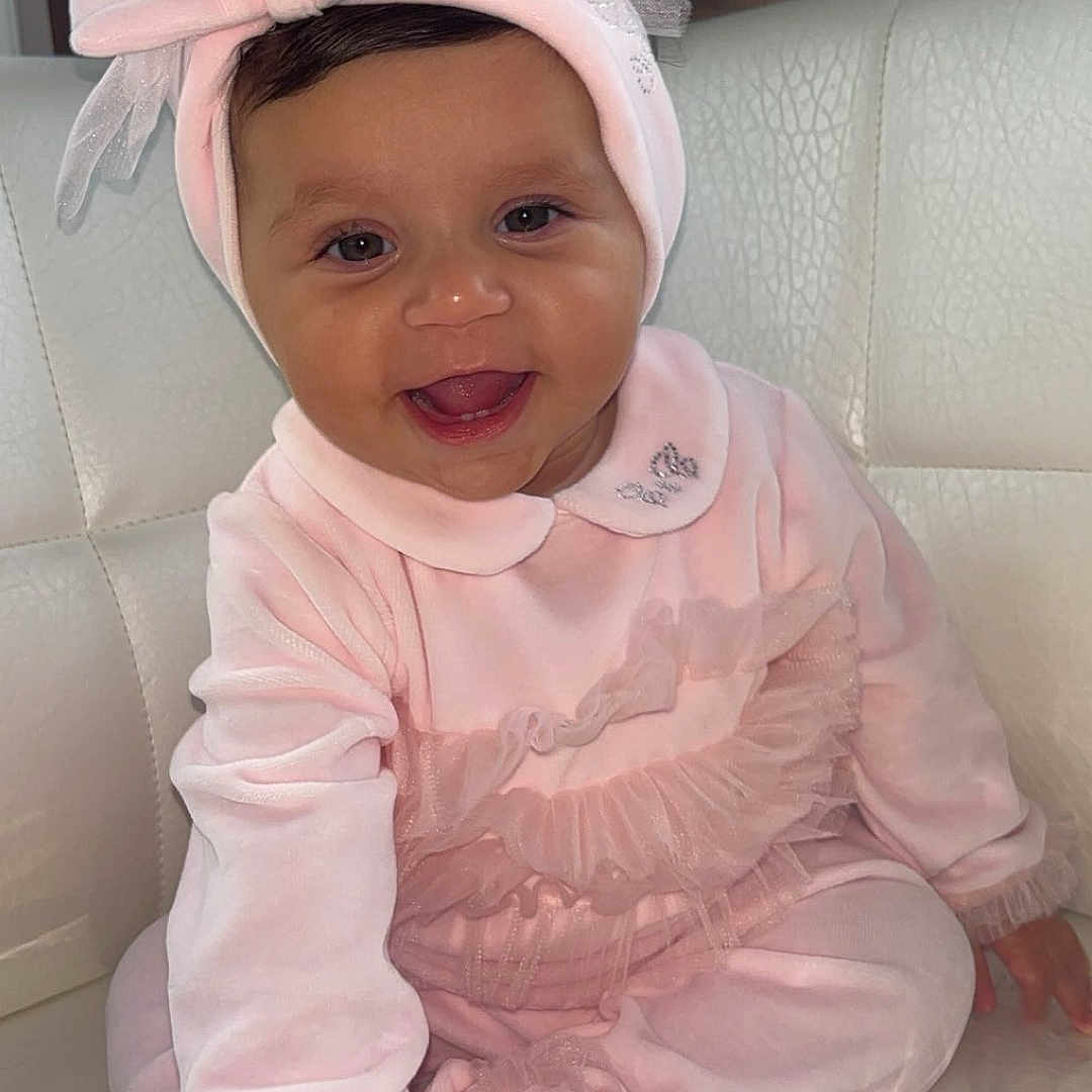 Noah participe au concours pour gagner de l'argent avec cette photo : baby, bow, child, couch, cute, face, furniture, hand, happy, headband, human, indoors, infant, pink_clothing, portrait, sitting, smiling, soft_fabric, toddler, white_cushion