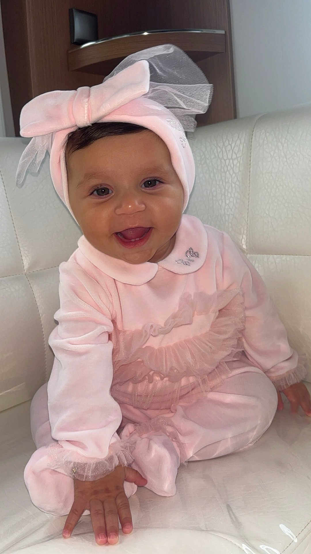 Noah participe au concours pour gagner de l'argent avec cette photo : baby, smiling, pink_clothing, headband, bow, infant, couch, white_cushion, hand, happy, indoors, face, child, sitting, cute, portrait, soft_fabric, furniture, toddler, human