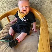 Xander Haze is registered to the contest to win money with this photo: baby, child, smile, black_clothing, yellow_bib, sitting, wooden_chair, cushion, shoe, sock, indoor, person, happy, cute, face, head, skin, texture, light, background