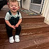 Harper is registered to the contest to win money with this photo: child, toddler, smiling, sitting, wooden_steps, outdoor, house, door, rug, earrings, white_shoes, green_overall, short_sleeve_shirt, happy, expression, person, casual_clothing, daylight, playful, portrait