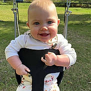 Kinsley is registered to the contest to win money with this photo: baby, child, swing, outdoor, grass, smiling, happy, face, person, playground, fence, sunlight, clothing, floral_pattern, seat, nature, daylight, cute, infant, park