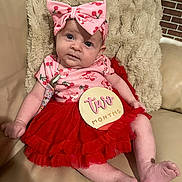 Amyra is registered to the contest to win money with this photo: baby, infant, child, pink_bow, cherry_pattern, red_skirt, two_months_sign, couch, beige, plush_blanket, cute, portrait, indoors, person, smiling, fashion, headband, sitting, happy, skin