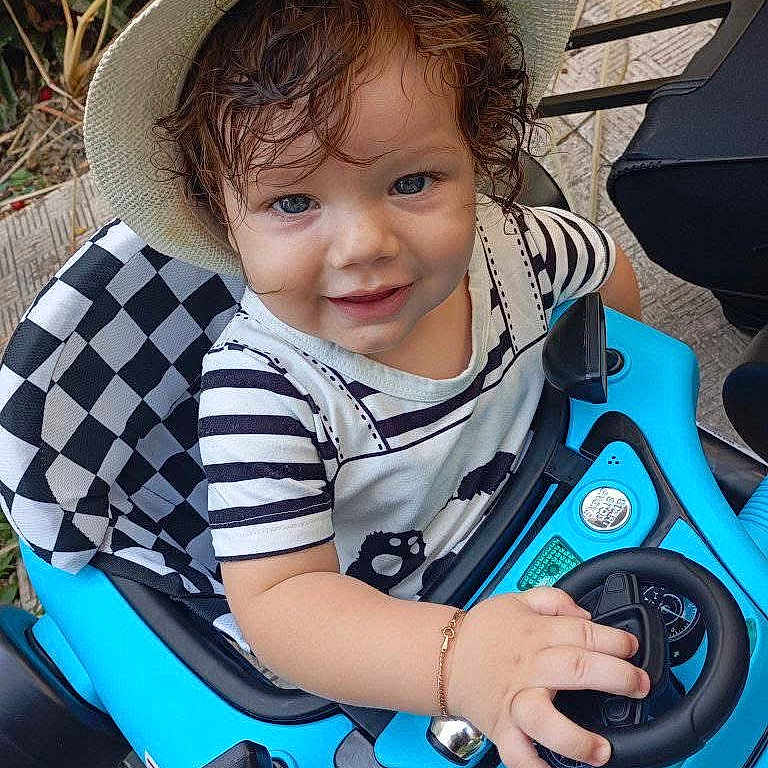 Demis joined the competition — help win amazing prizes! blue, bracelet, child, curly_hair, cute, daytime, fun, happy, hat, outdoor, person, play, seat, smiling, steering_wheel, striped_shirt, toddler, toy_car, vehicle, young_child
