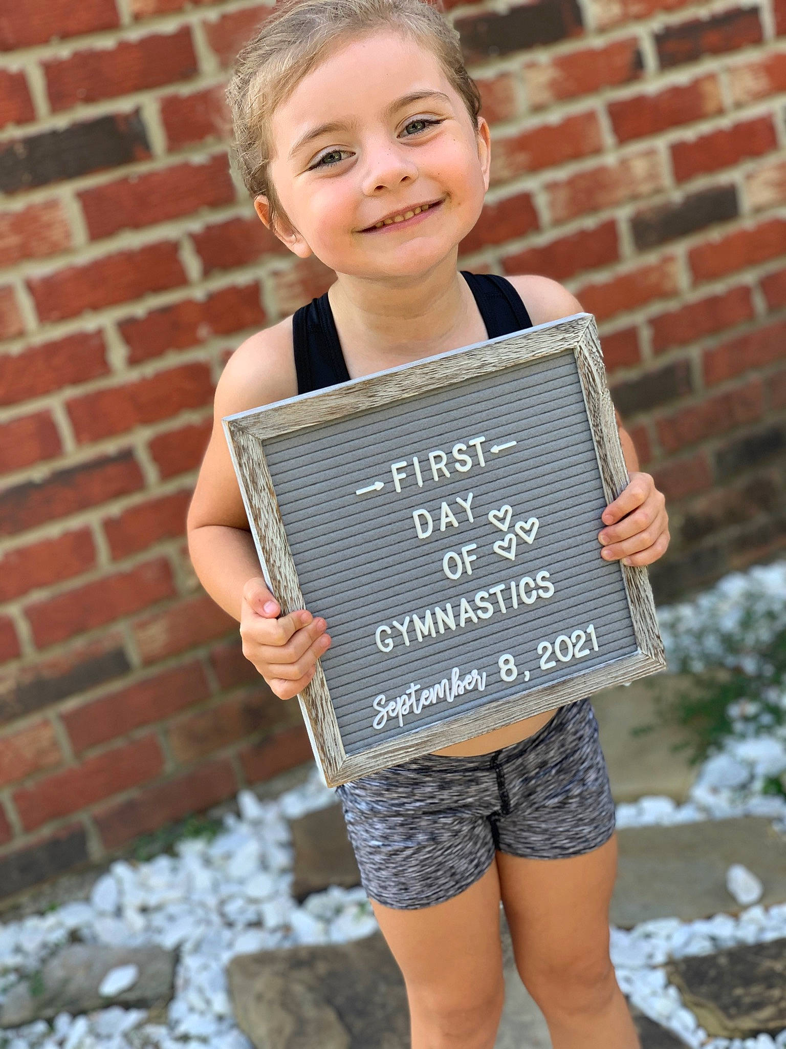 Emmalyn is registered to the contest to win money with this photo: brick, brickwork, child, clothing, face, facial_expression, hair, hairstyle, hand, happy, joy, organ, outerwear, person, photograph, plant, shoulder, sleeve, smile, street_fashion