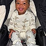baby, child, smiling, pajamas, teddy_bear_pattern, white_booties, car_seat, happy, cute, indoor, infant, clothing, face, person, seatbelt, black_hair, small_hands, cozy, warm, adorable