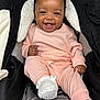 baby, smiling, pink_clothing, knitwear, white_booties, stroller, black_stroller, fleece_lining, happy, infant, cute, child, seated, portrait, cozy, indoors, face, small_hands, footwear, warm