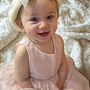 River is registered to the contest to win money with this photo: baby, child, smile, pink_dress, white_hat, bow, face, eyes, cheeks, sitting, blanket, soft_texture, cute, portrait, infant, happy, indoors, clothing, headwear, person