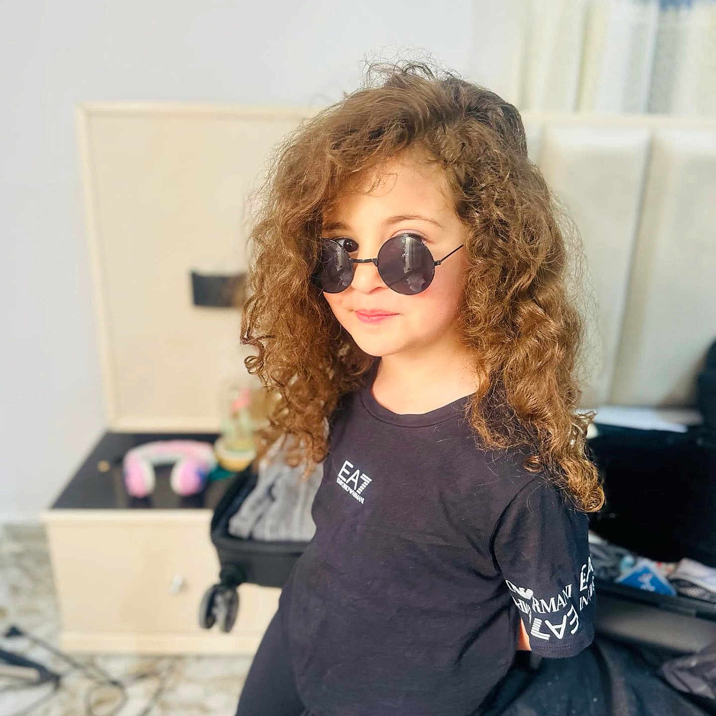 Hadjira participe au concours pour gagner de l'argent avec cette photo : bedroom, black_clothing, casual, child, cool, curly, curly_hair, fashion, furniture, hair, headphones, indoor, nightstand, person, portrait, relaxed, smile, suitcase, sunglasses, young