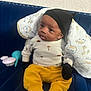 Ahmir Lamelo is registered to the contest to win money with this photo: baby, infant, child, couch, blue_couch, blanket, hat, mittens, yellow_pants, white_socks, toy, baby_toys, patterned_blanket, seated, indoor, curious, portrait, clothing, face, person