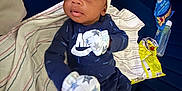 Ahmir Lamelo is registered to the contest to win money with this photo: baby, infant, blanket, pacifier, baby_bottle, snack, mittens, onesie, hat, couch, striped_blanket, blue_cushion, person, indoor, clothing, food, tableware, young_child, cute, relaxing