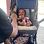 adult, baby, bag, brick_wall, casual_clothing, child, comfort, concrete, footwear, hand, happiness, infant, mickey_mouse, outdoor, parent, person, seat, smile, stroller, sunlight