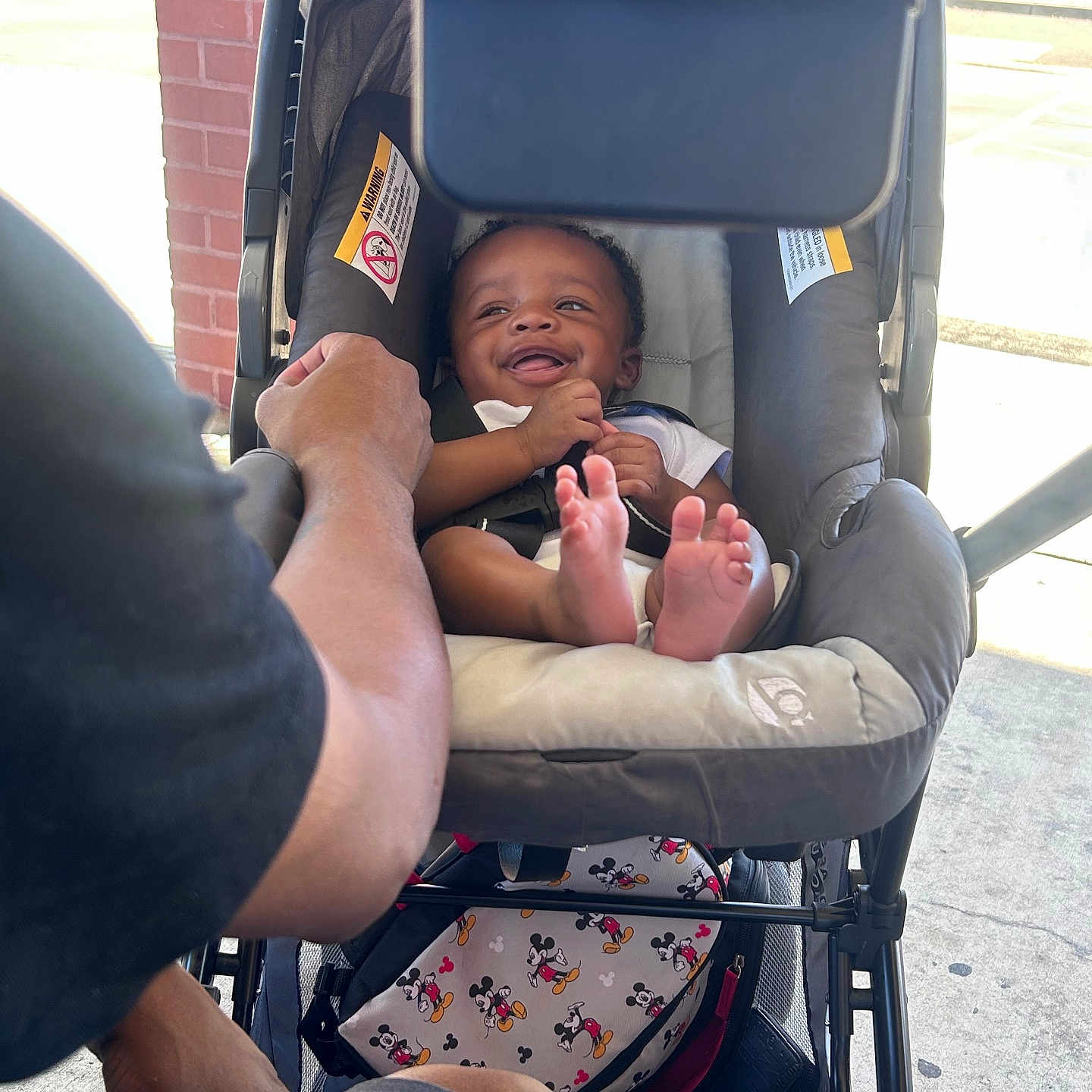 Ahmir Lamelo is registered to the contest to win money with this photo: adult, baby, bag, brick_wall, casual_clothing, child, comfort, concrete, footwear, hand, happiness, infant, mickey_mouse, outdoor, parent, person, seat, smile, stroller, sunlight