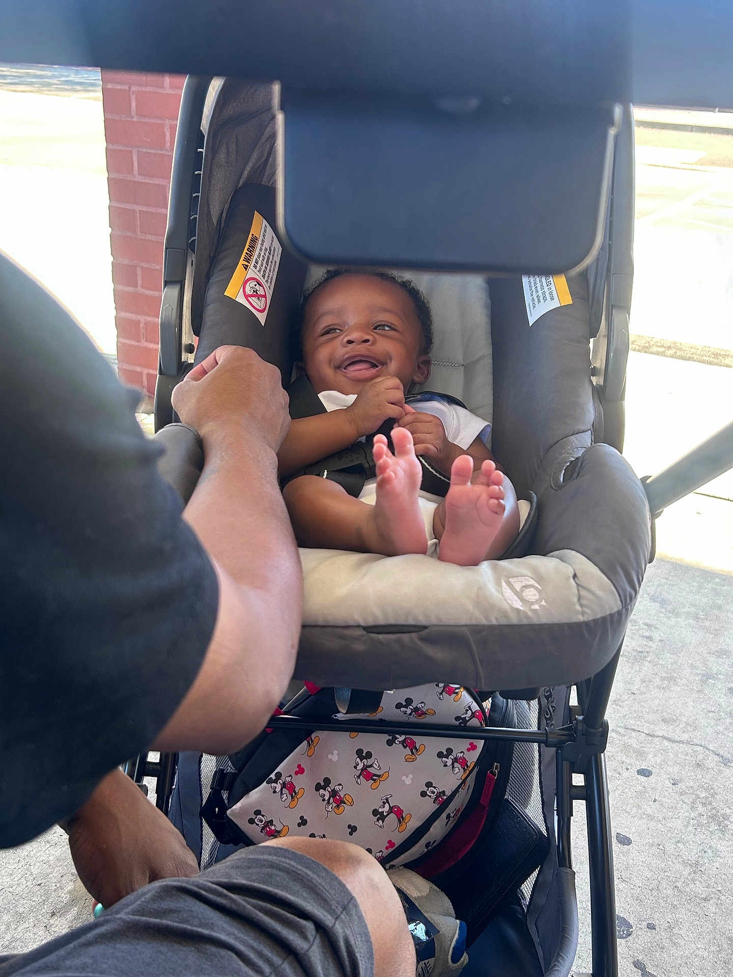 Ahmir Lamelo is registered to the contest to win money with this photo: adult, baby, bag, brick_wall, casual_clothing, child, comfort, concrete, footwear, hand, happiness, infant, mickey_mouse, outdoor, parent, person, seat, smile, stroller, sunlight