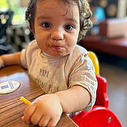 Hélio Et Ezio a rejoint le concours — aidez-le/la à gagner de superbes lots ! toddler, child, face, food, messy_face, high_chair, french_fry, hand, table, indoor, curly_hair, person, casual_clothing, cute, eating, restaurant, blurred_background, expression, young_child, seat