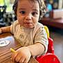 toddler, child, face, food, messy_face, high_chair, french_fry, hand, table, indoor, curly_hair, person, casual_clothing, cute, eating, restaurant, blurred_background, expression, young_child, seat