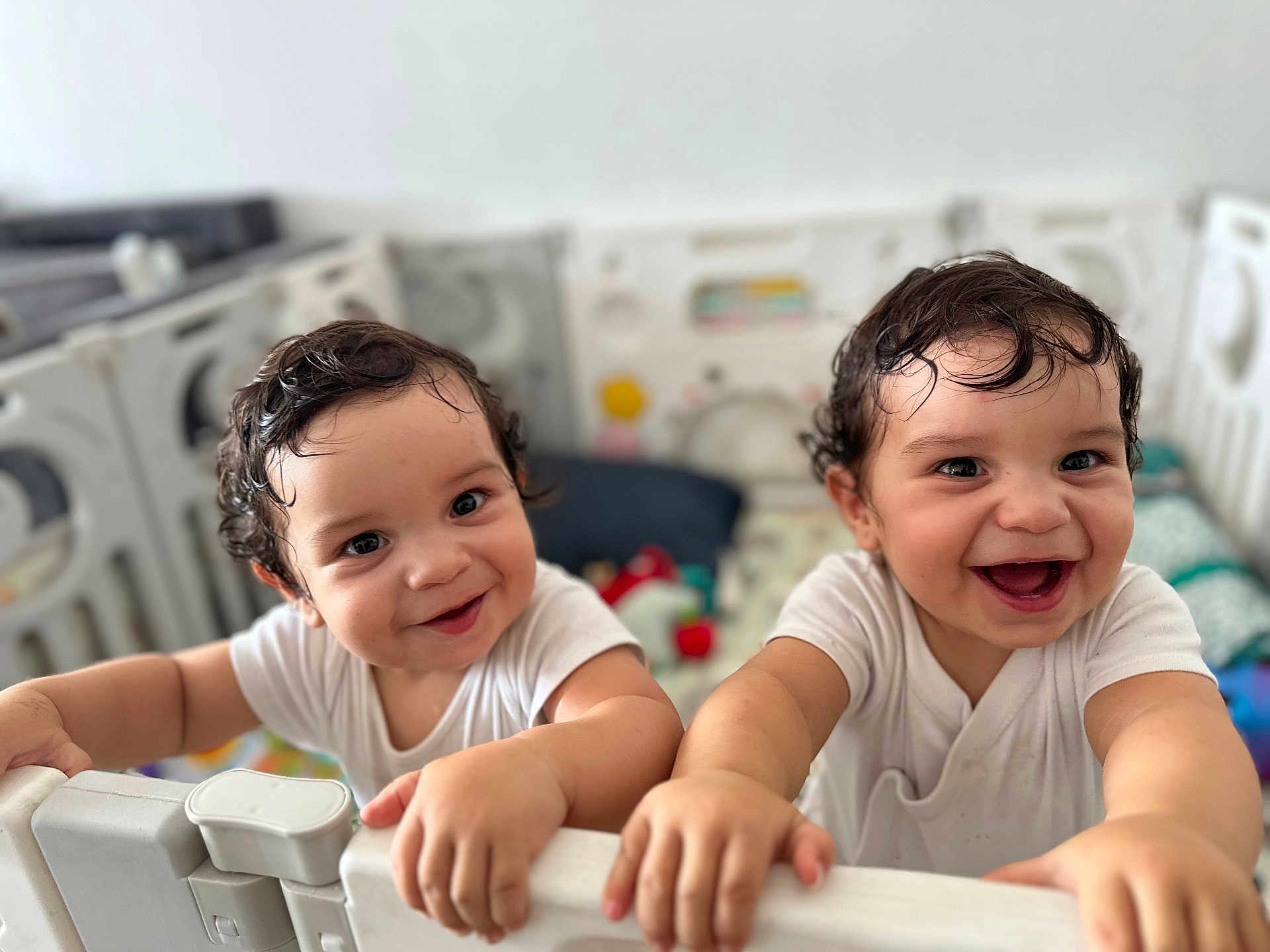 Hélio Et Ezio participe au concours pour gagner de l'argent avec cette photo : child, toddler, baby, playpen, smiling, happy, curly_hair, white_clothing, indoor, face, hands, cute, joyful, playful, infant, two_children, closeup, expression, young, person