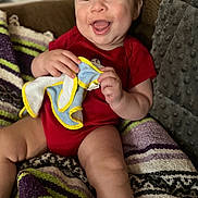 Daniel is registered to the contest to win money with this photo: baby, blanket, child, comfort, cute, expression, face, hand, happy, human, indoors, infant, portrait, red_onesie, seated, skin, smiling, soft_cloth, striped_blanket, texture