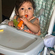Jesus Ismael joined the competition — help win amazing prizes! baby, child, high_chair, eating, carrot, spoon, smiling, sitting, portrait, indoors, kitchen, mealtime, infant, toddler, bib, seatbelt, tray, food, curious, 家庭