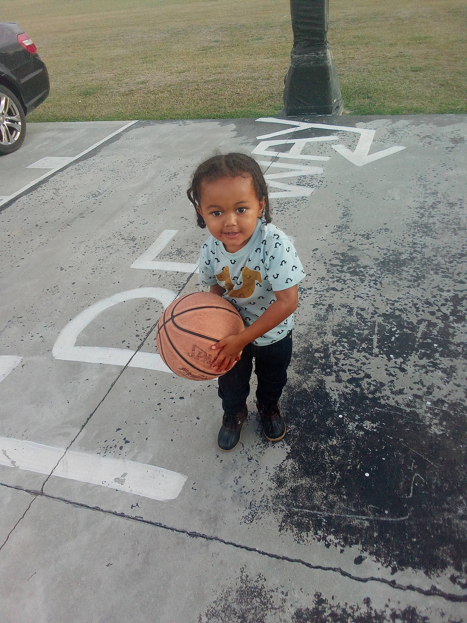 Brandon is registered to the contest to win money with this photo: asphalt, automotive_tire, ball, basketball, child, city, concrete, fun, grass, person, play, road, road_surface, sidewalk, sitting, sports_equipment, street, streetball, tire, toddler