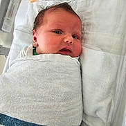 Elodie is registered to the contest to win money with this photo: baby, newborn, infant, wrapped, blanket, bed, pacifier, lying_down, face, head, skin, curly_hair, indoors, soft_light, white_bedding, cute, sleepy, person, child, newborn_baby