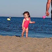 June participe au concours pour gagner de l'argent avec cette photo : child, toddler, beach, sand, water, ocean, swimsuit, pink, sunny, daytime, person, adult, toy, sand_toy, outdoor, sky, waves, happy, hair, summer