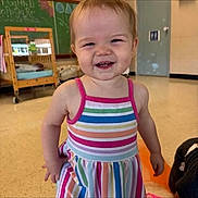 Laney joined the competition — help win amazing prizes! toddler, child, smiling, dress, striped_clothing, indoor, classroom, crib, chalkboard, floor, person, happy, young_child, playful, cute, standing, short_hair, earrings, colorful, casual