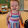 toddler, child, smiling, dress, striped_clothing, indoor, classroom, crib, chalkboard, floor, person, happy, young_child, playful, cute, standing, short_hair, earrings, colorful, casual