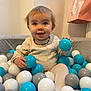 Manel a rejoint le concours — aidez-le/la à gagner de superbes lots ! baby, child, ball_pit, toys, balls, smiling, happy, indoor, person, play, sitting, clothing, necklace, white_balls, gray_balls, blue_balls, pink_bag, wall, cute, portrait