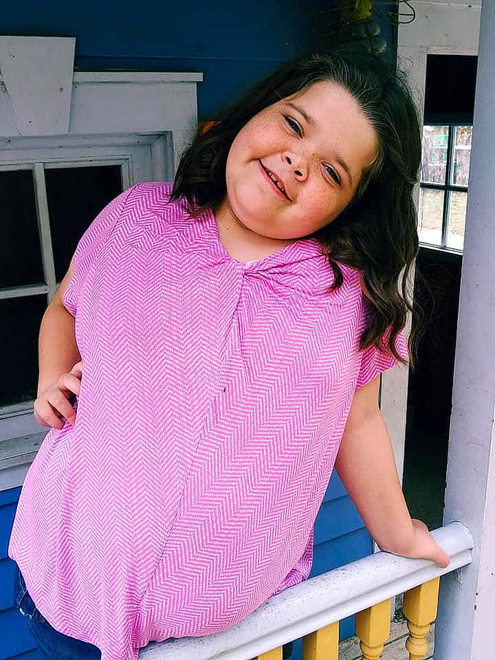 Hannah is registered to the contest to win money with this photo: abdomen, black_hair, child, joy, leg, neck, person, pink, shoulder, sitting, smile, textile, thigh, trunk