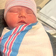 Gracie is registered to the contest to win money with this photo: baby, newborn, infant, swaddle, hospital_blanket, striped_hat, sleeping, closeup, portrait, face, mouth, nose, cheeks, skin, curtain, bassinet, blanket, arm, bed, cozy