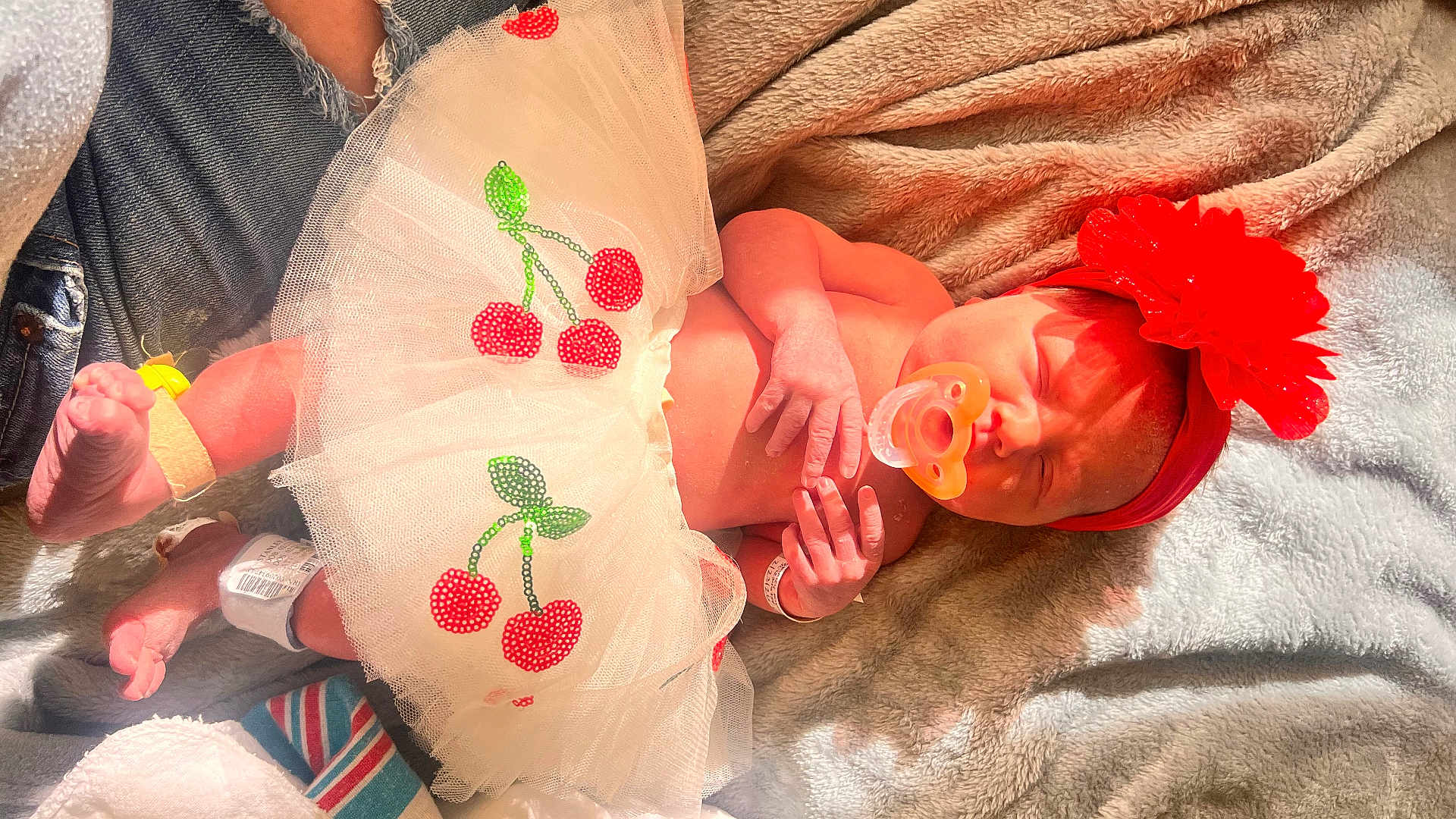 Gracie is registered to the contest to win money with this photo: newborn, baby, pacifier, red_headband, flower_headband, tutu, cherry_applique, blanket, sleeping, bare_skin, hospital_id_band, tiny_feet, toes, jeans, adult_leg, plush, cotton, hospital_towel, closeup, portrait