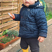 Duarte a rejoint le concours — aidez-le/la à gagner de superbes lots ! toddler, child, yellow_boots, rain_boots, navy_jacket, outdoor, garden, wooden_fence, hose, pavement, person, clothing, serious, holding_object, plant_pot, greenery, casual, young_child, standing, curly_hair