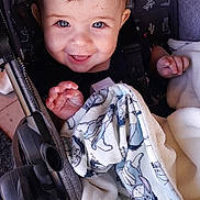 Sylas is registered to the contest to win money with this photo: baby, child, smiling, stroller, blanket, blue_eyes, happy, infant, cute, clothing, person, portrait, seated, cartoon, fabric, hand, head, face, indoor, cozy