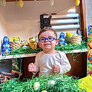 Maélän a rejoint le concours — aidez-le/la à gagner de superbes lots ! child, toddler, eyeglasses, blue_glasses, easter, easter_egg, easter_basket, chocolate_bunny, foil_wrapping, decorative_grass, green_grass, smiling, portrait, indoor, shelf, toys, plush_chick, painted_egg, cardboard_box, festive