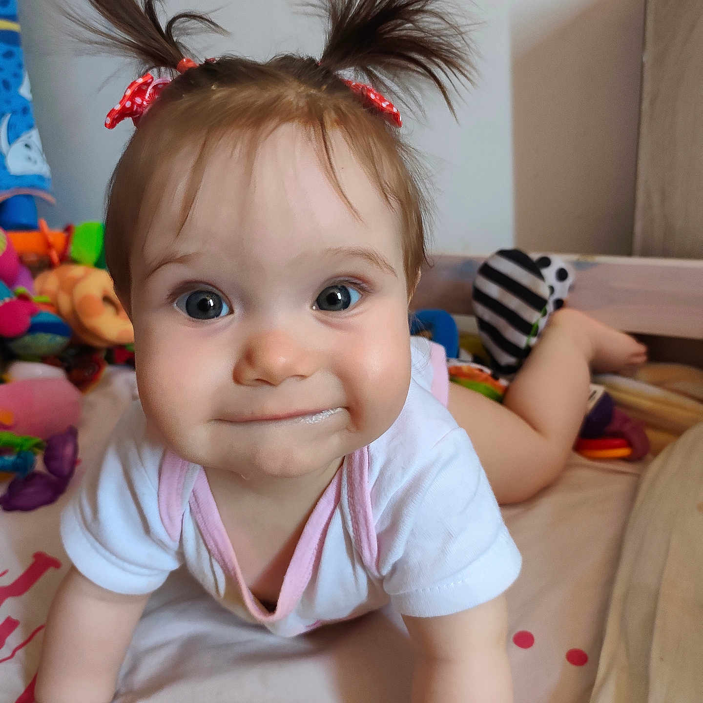 Azurhya participe au concours pour gagner de l'argent avec cette photo : baby, bed, child, clothing, crawling, curious, cute, expression, face, feet, hands, indoor, person, pigtails, pink_trim, playful, red_bows, smile, toys, white_shirt